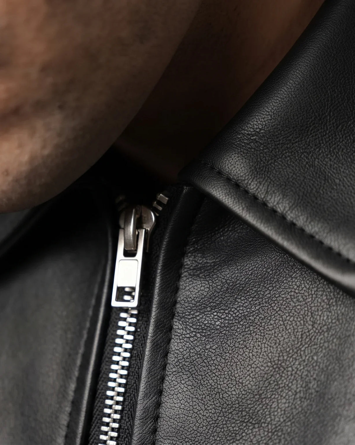 Close-up of a black faux leather jacket collar and metal zip