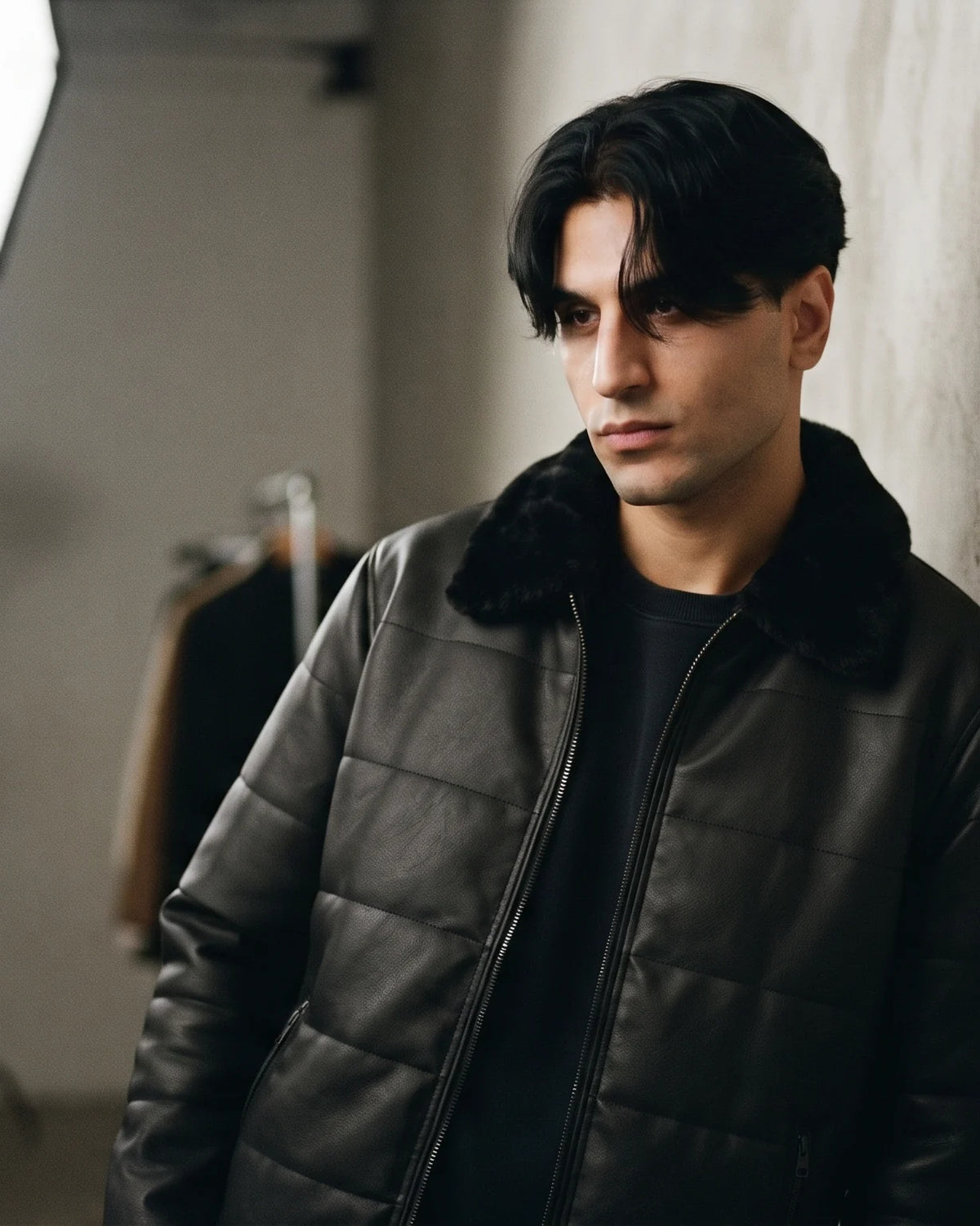 Zaryash black faux leather bomber jacket, leaning on a wall